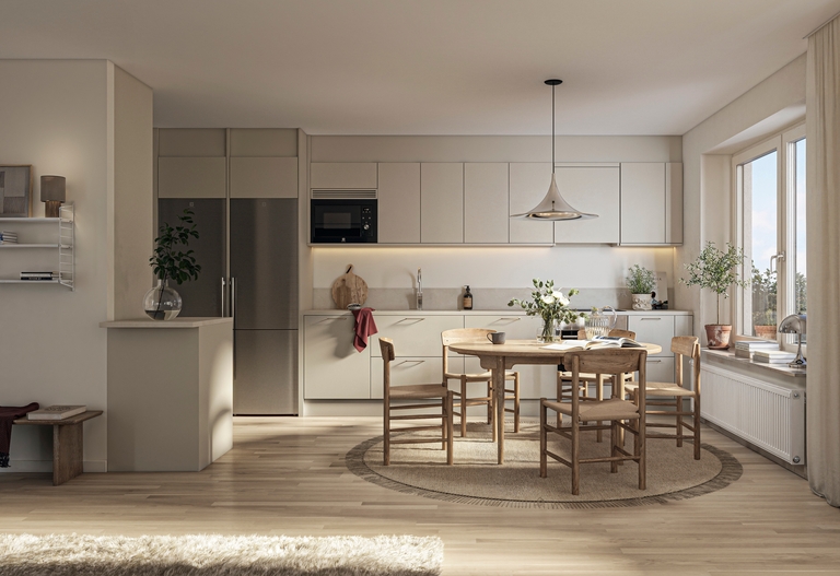 Ljust kök med rostfria vitvaror längs en vägg. Framför står ett runt matbord med fem stolar, precis vid övergången till ett vardagsrum.