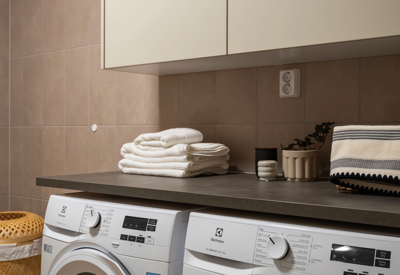Del av badrum med tvättmaskin, torktumlare, vikta handdukar och förvaringskärl på en bänkskiva.