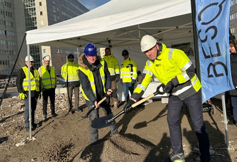 Magnus och Anders tar första spadtaget för Glimten. De är omgivna av andra under ett tält, med en flagga märkt "BESQAB" i närheten.