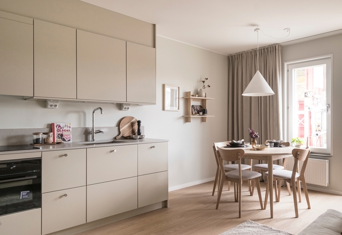 Modernt kök med beige skåp, ett litet matbord med fyra stolar och ett fönster som släpper in naturligt ljus.