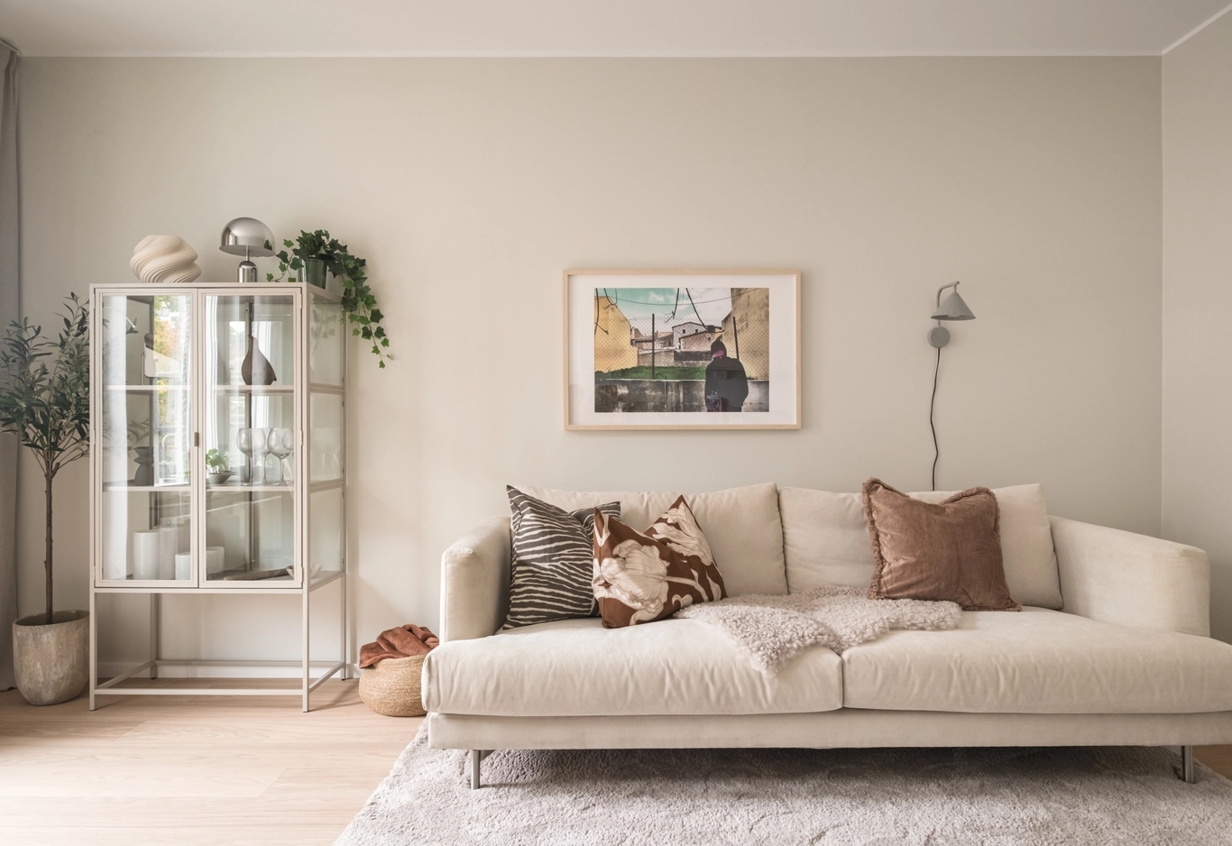 Glasskåp med fina saker i intill en bäddsoffa med kuddar.