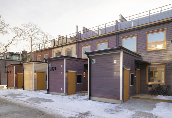 Rad av moderna radhus i tre våningar med entréer, platta tak och snö på marken.