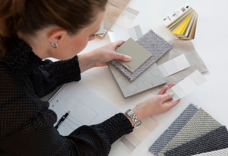 En kvinna som håller olika materialprover i sin hand över ett bord.