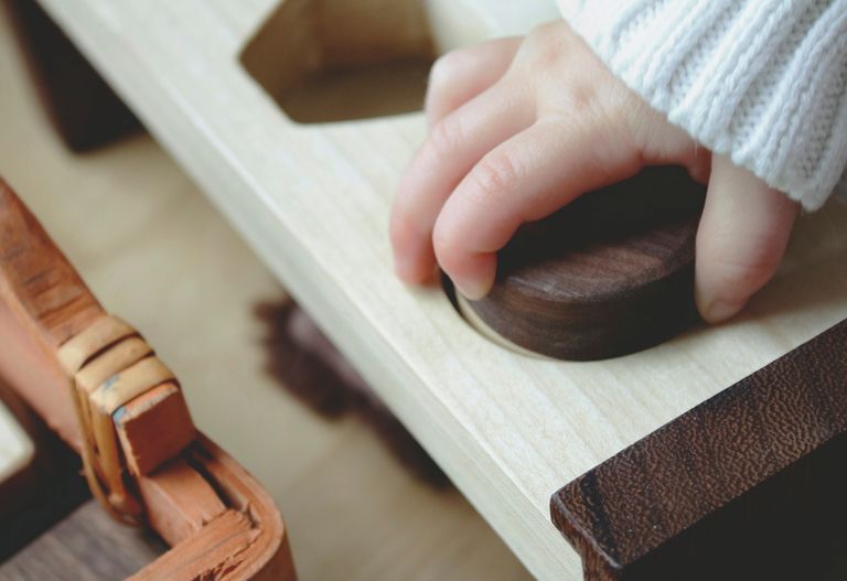 Ett barns hand placerar en rund träpinne i ett matchande hål på en ljus träskiva.