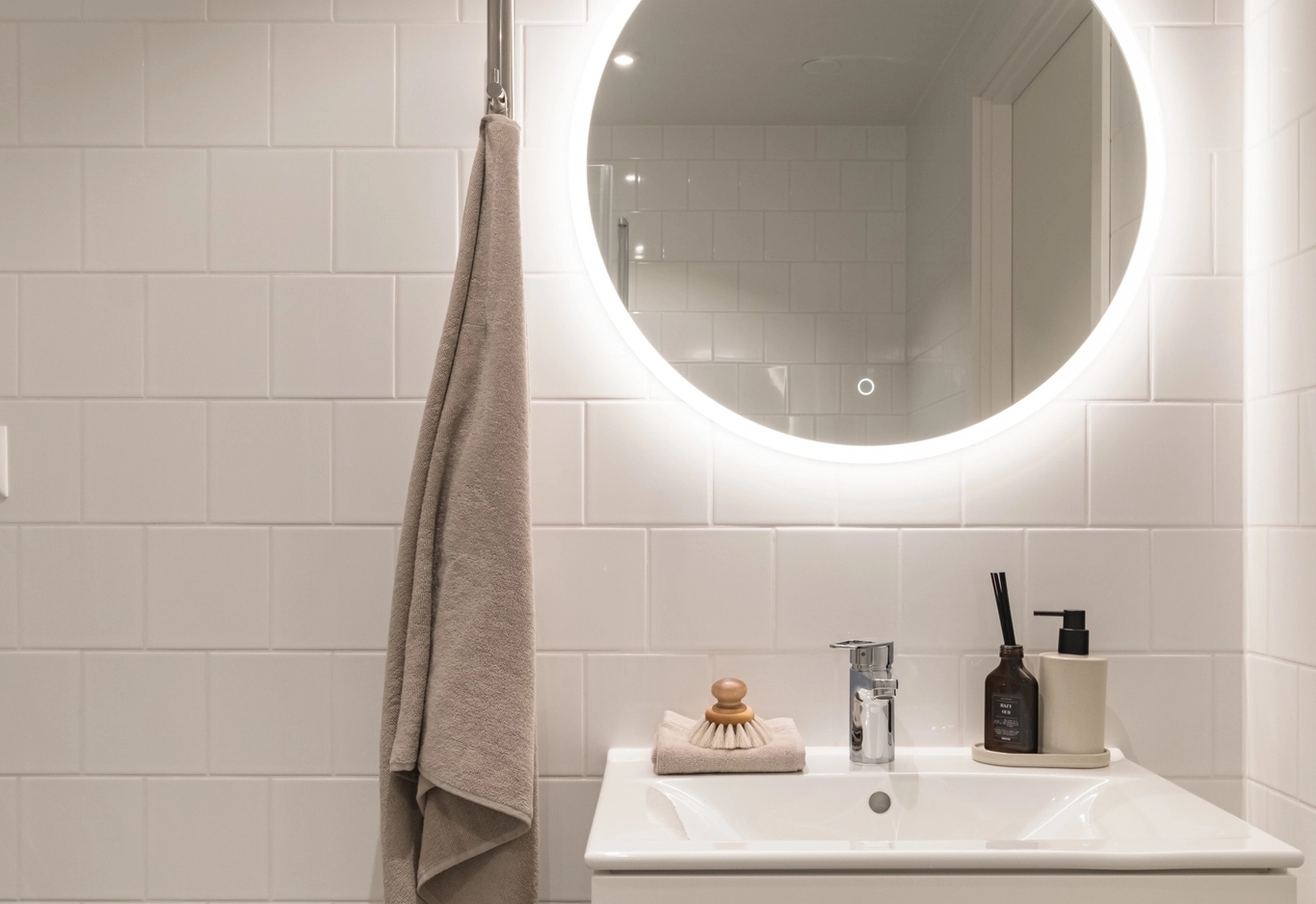 Rund spegel med belysning bakom i ett badrum med kaklade väggar i beige.