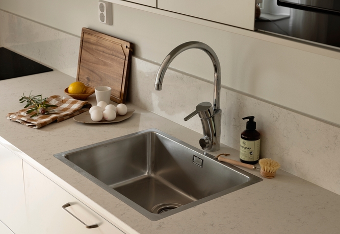 En modern diskbänk med kran, tvålpump och bänkskivor med bland annat ägg, citron och en skärbräda.