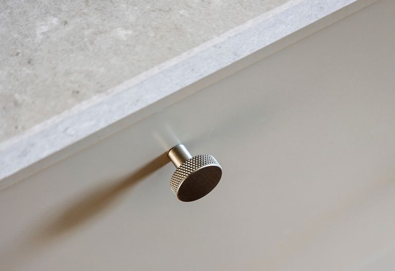 Närbild av en metallisk rund lådknopp fäst vid en ljus låda med en texturerad bänkskiva ovanför.