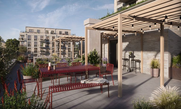 Gemensam takterrass med bänkar, bord, pergola, krukväxter och ljusslingor. En flervåningsbyggnad syns i bakgrunden.