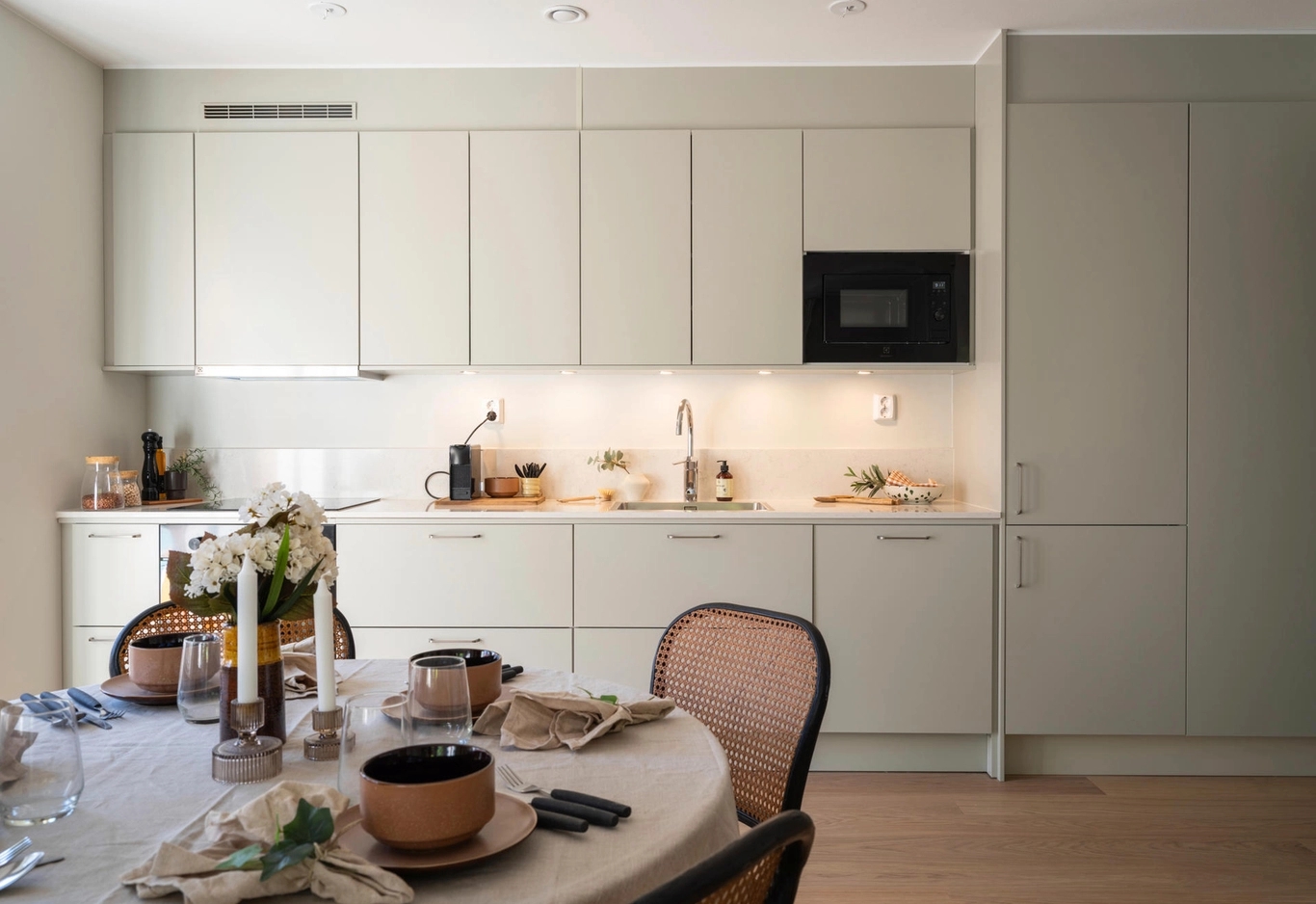 Modernt kök och matplats med neutrala toner, sittö och stora fönster som släpper in naturligt ljus.
