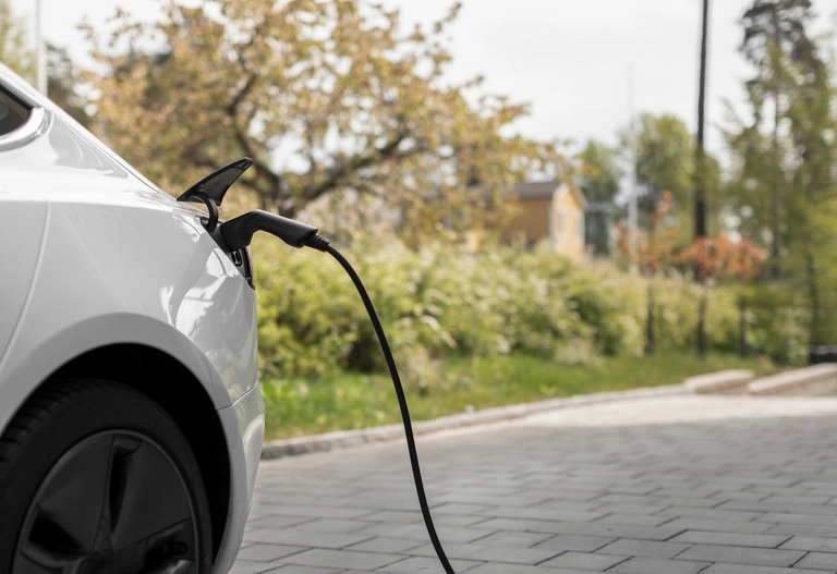 En vit elbil står parkerad på en asfalterad yta och inkopplad till en laddstation utomhus.