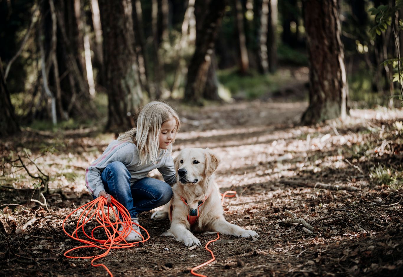 Ett barn sitter på knä bredvid en hund som ligger på en skogsstig.