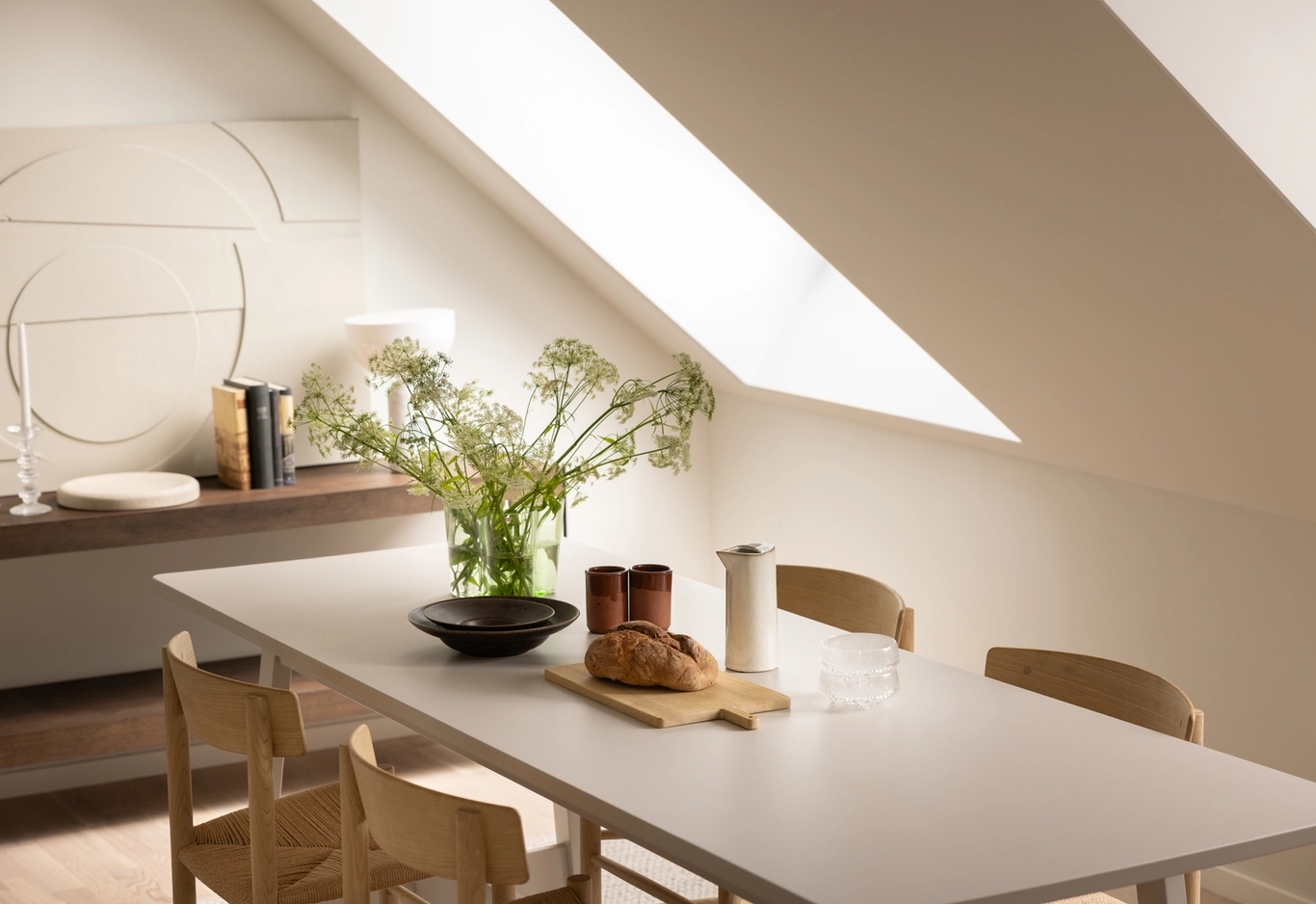 Matplats under snedtak möblerad med matbord med plats för 4-6 personer. På bordet står en vas med blommor och på bordet ligger en skärbräda med ett surdegsbröd.