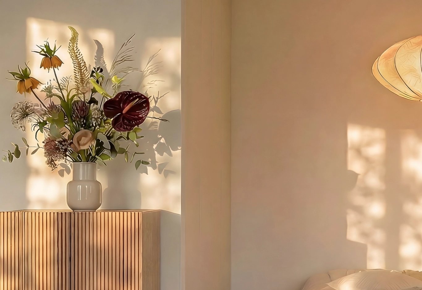 Stor blomsterbukett i vas på ribbad träskänk. Solljus skapar långa skuggor på väggen i ett varmt rum.