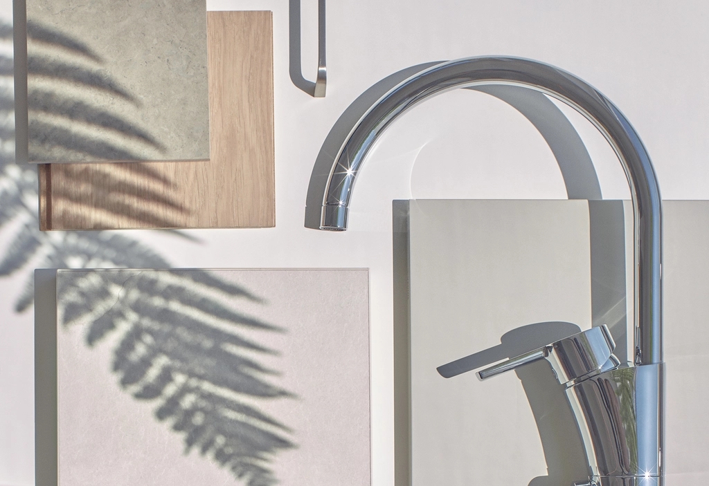 Moodboard över materialval i en nyproducerad bostad. En modern kran i krom tillsammans med rektangulära prover och en skugga av ett ormbunksblad mot en vit bakgrund.