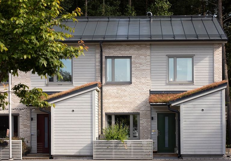 Två moderna radhus med ljus tegel- och träfasad, sneda tak och små inhägnade framgårdar.