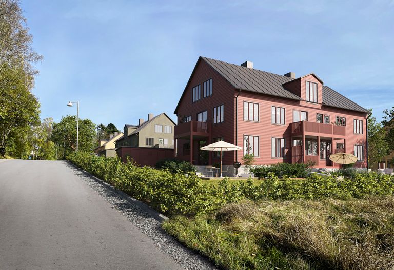 Ett rött hus med mörkt tak, omgivet av grönska. En väg är till vänster, och det finns några andra hus i bakgrunden.