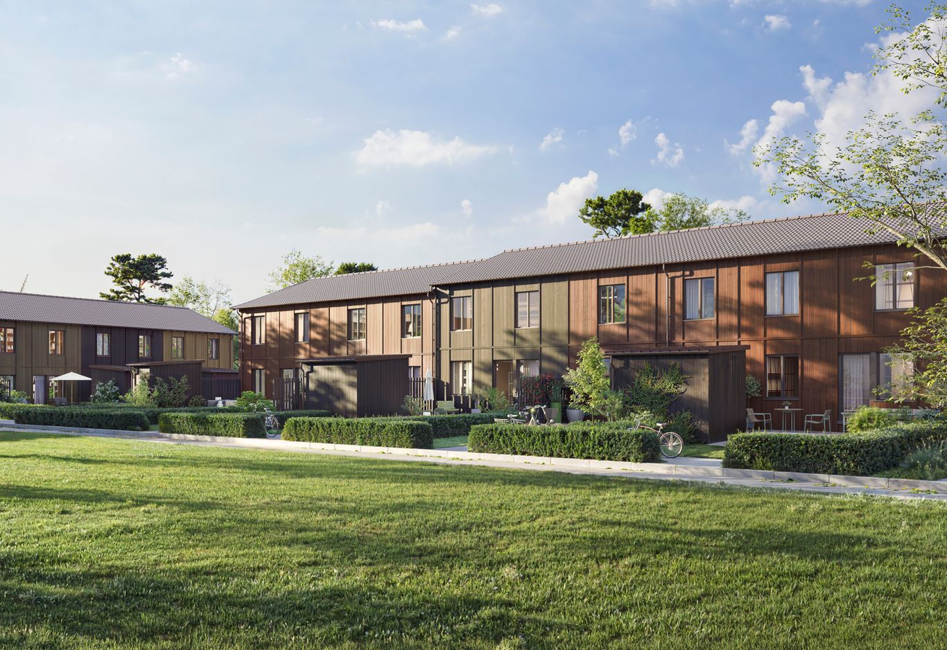 Gräsmatta och gångväg framför tvåvånings träbyggnader med stora fönster, omgiven av träd.