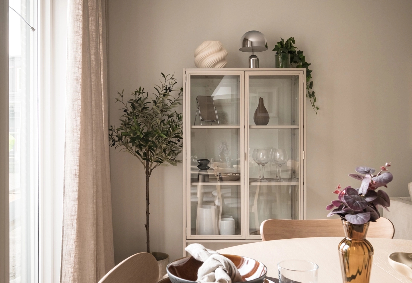 Ett skåp med fin inredning i, tillsammans med växter bakom ett matbord.