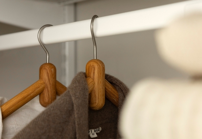 Två klädhängare i trä med bruna plagg hänger på en vit garderobsstång.