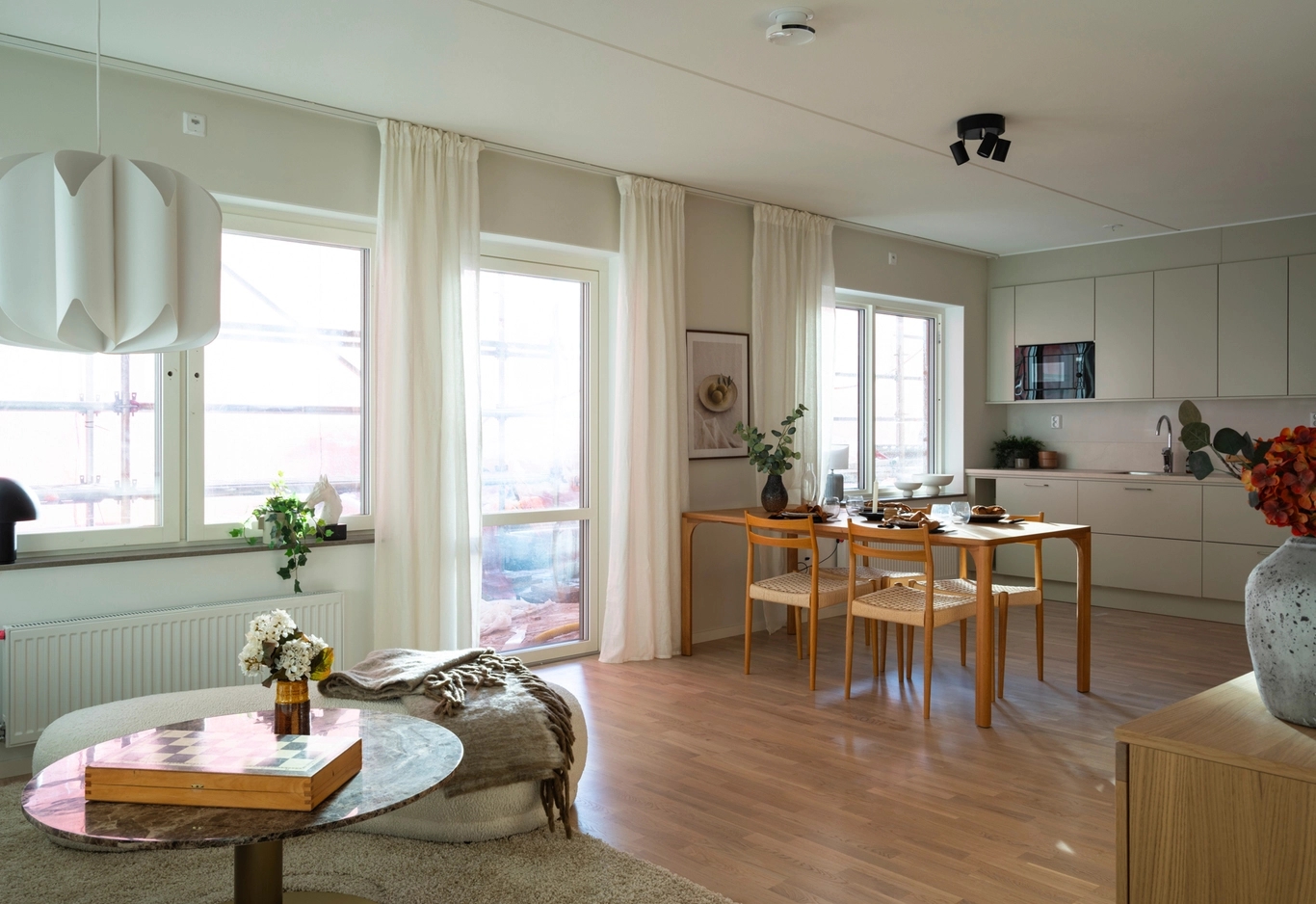 Ljust, modernt kök och matplats med stora fönster, ljust trägolv och enkel, minimalistisk inredning.