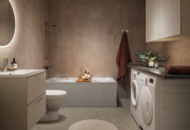 Helkaklat badrum med dämpad belysning och tända ljus. Ett badkar är fyllt med badskum. I förgrunden syns en kommod och tvättmaskin och torktumlare.