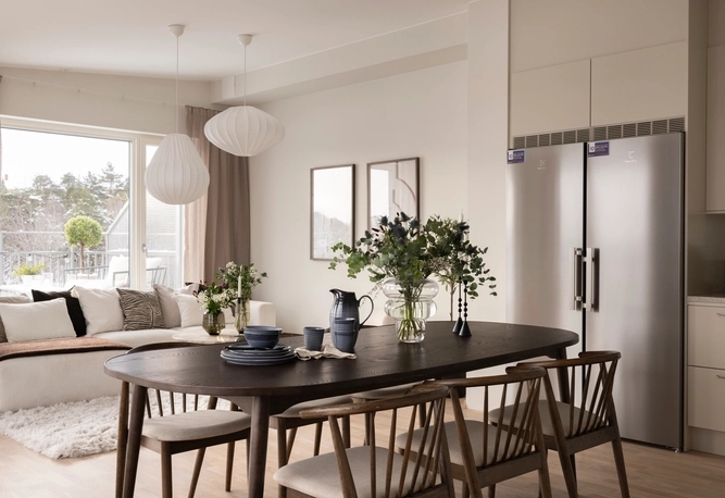 Modern matplats med bord och stolar i mörkt trä och modern inredning intill ett ljust vardagsrum och kök.