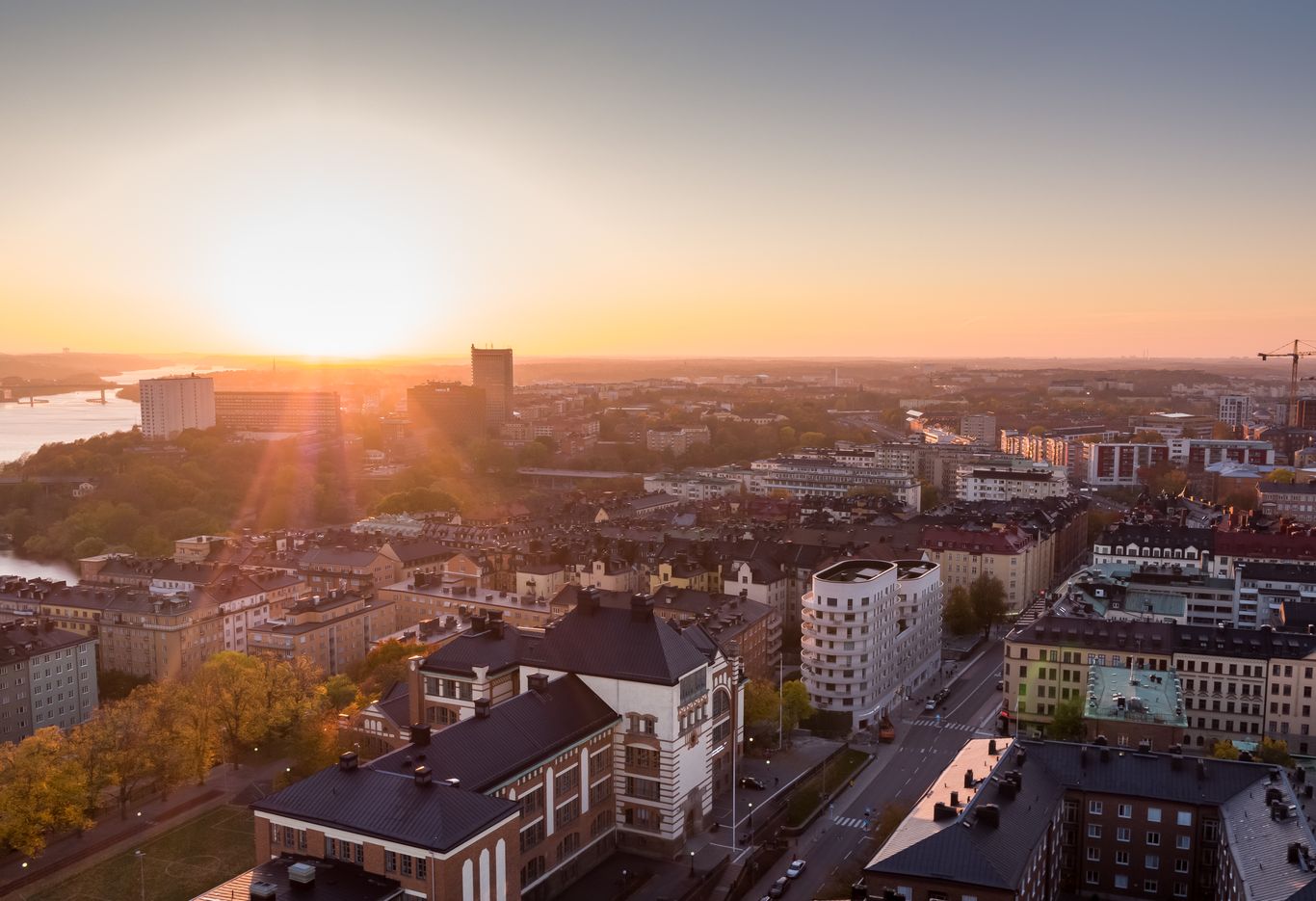 Flygfoto över en stadsbild vid solnedgången, med solljus som lyser upp byggnader och gator.